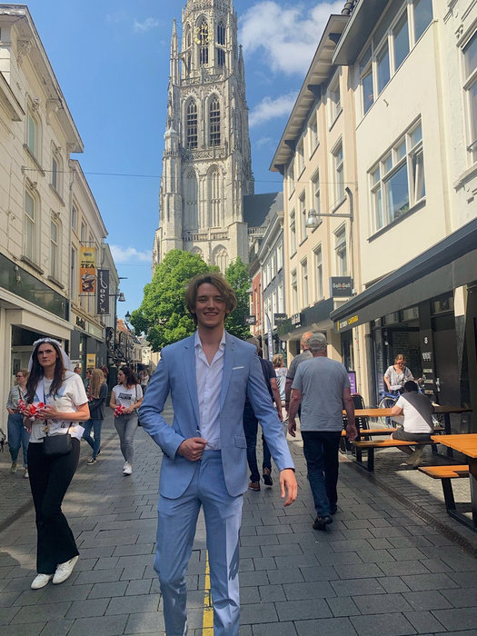 Kees in a light blue suit walking down a shopping street, smiling